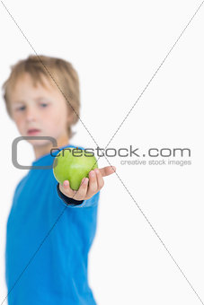 Young boy holding out a green apple
