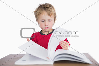 Little boy sitting at desk and reading book