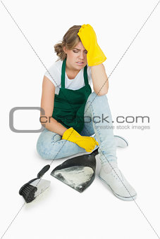 Tired young maid sitting with brush and dust pan