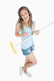 Woman playing air guitar with broom while listening music over headphones