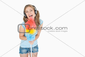 Woman holding feather duster as microphone and listening music over headphones