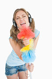 Woman holding feather duster as microphone and listening music over headphones