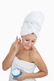 Woman wrapped in towel applying cream on face over