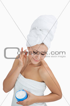Woman wrapped in towel applying cream on face over