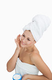 Happy woman wrapped in towel applying cream on face