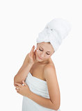 Woman wrapped in towel applying cream on face