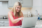 Happy young woman using laptop in kitchen