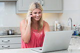 Happy woman using laptop while on call in the kitchen