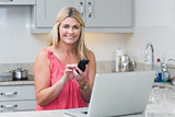 Woman text messaging while using laptop in the kitchen