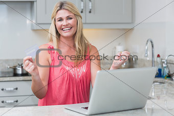 Excited woman with clenched fists using laptop in the kitchen