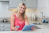 Woman holding credit card and digital tablet in kitchen