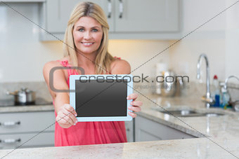 Portrait of casual woman holding out digital tablet in kitchen
