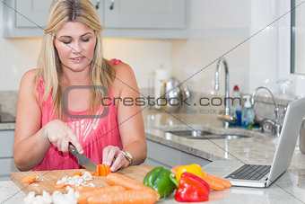 Woman making recipe from internet on laptop in kitchen
