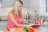 Woman reading cookbook book while cutting vegetables in kitchen