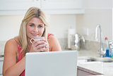 Woman with coffee cup and laptop in the kitchen