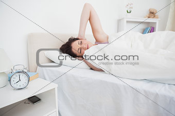 Woman covering ears in bed as alarm clock rings