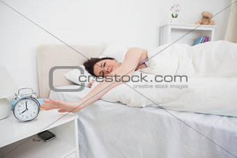 Sleepy woman extending hand to alarm clock