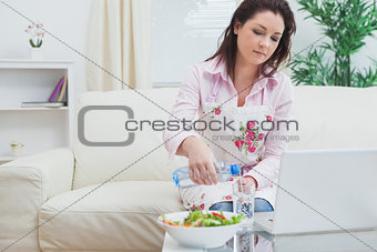 Woman with salad and laptop while pouring water in glass at home