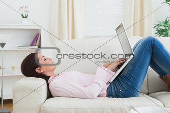 Casual woman lying on sofa and using laptop