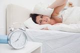 Woman covers ears with pillow as alarm clock rings