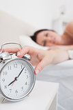 Woman in bed extending hand to alarm clock