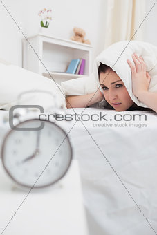 Woman covers ears with sheet as alarm clock rings