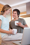 Couple looking at each with coffee cups while using laptop