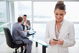 Colleagues in meeting with business woman text messaging in foreground