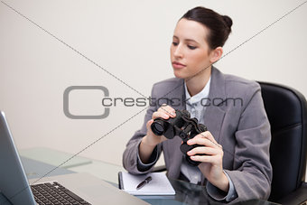 Business woman with binoculars looking at laptop