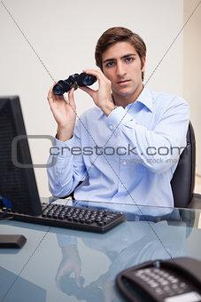 Business man with binoculars sitting at office desk