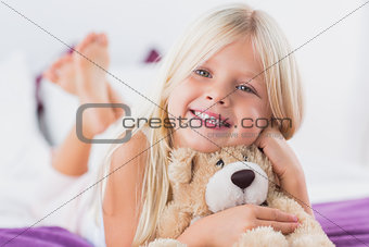 Little girl with her teddy bear lying on a bed