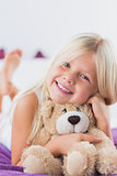 Smiling girl with her teddy bear lying on a bed