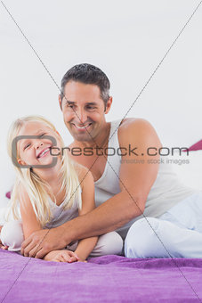 Smiling father and his daughter sitting on a bed