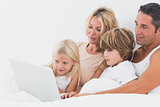 Family watching a laptop screen on a bed