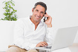 Smiling man using his laptop and phoning