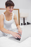 Happy woman using laptop in bed