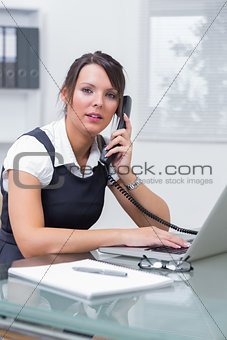 Female executive with laptop using landline phone at office