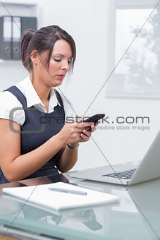 Business woman text messaging in front of laptop at office