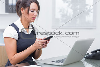 Business woman text messaging in front of laptop
