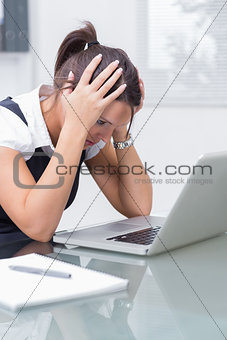 Business woman with head in hands in front of laptop at desk