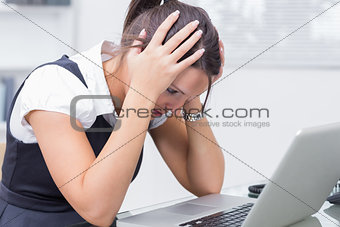 Frustrated business woman with head in hands in front of laptop at desk