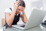 Upset business woman with head in hands in front of laptop at office
