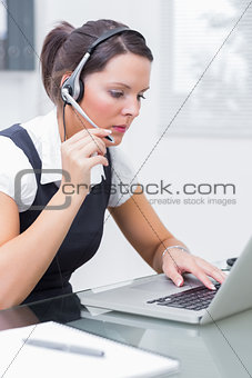 Business woman wearing headset and using laptop at desk