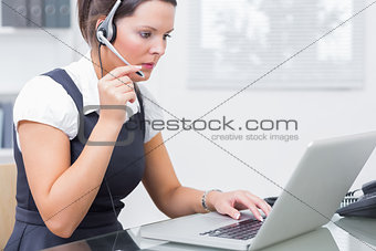 Business woman wearing headset and using laptop at office