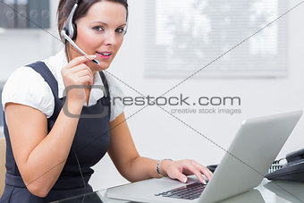 Female executive wearing headset while using laptop at desk