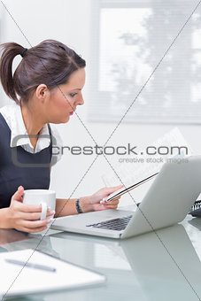 Executive with coffee cup and laptop reading paper at office