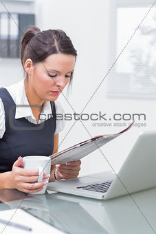 Business woman with coffee cup and laptop reading paper at office