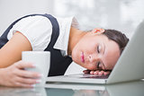 Business woman with coffee cup resting head on laptop at office