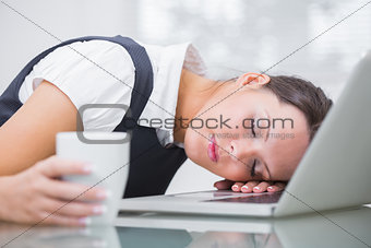 Business woman with coffee cup resting head on laptop at office