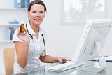 Portrait of female doctor holding medicine bottle in front of computer